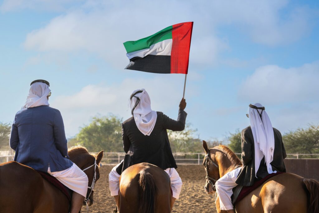 Riders in traditional dress on horseback carrying the UAE flag